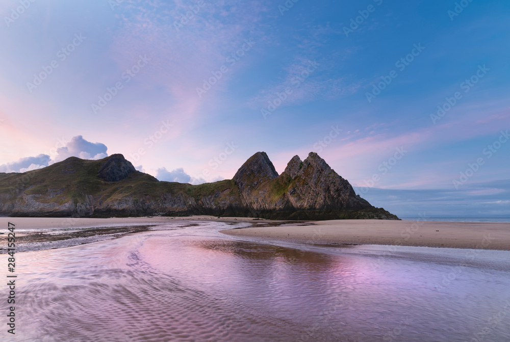 Beautiful colorful Summer sunrise landscape image of Three Cliffs Bay in South Wales