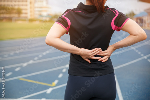 Female runner athlete back injury and pain. Woman suffering from painful lumbago while running on the blue rubberized running track.