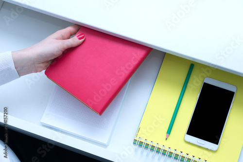 Office worker holding a red notebook, Desk, smart phone, open shelf, female hand, close up, top view, background, copy space, advertising