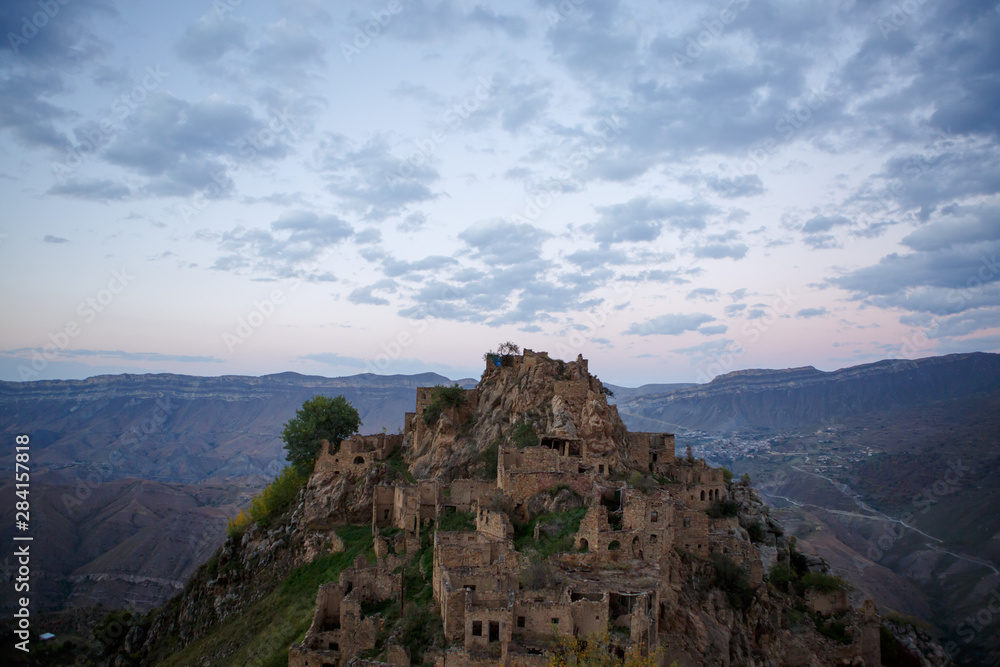 Photo of old ruins of mountain area with green vegetation against cloudy blue sky at sunset