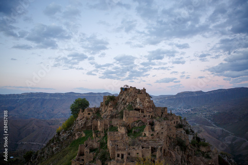 Photo of old ruins of mountain area with green vegetation against cloudy blue sky at sunset
