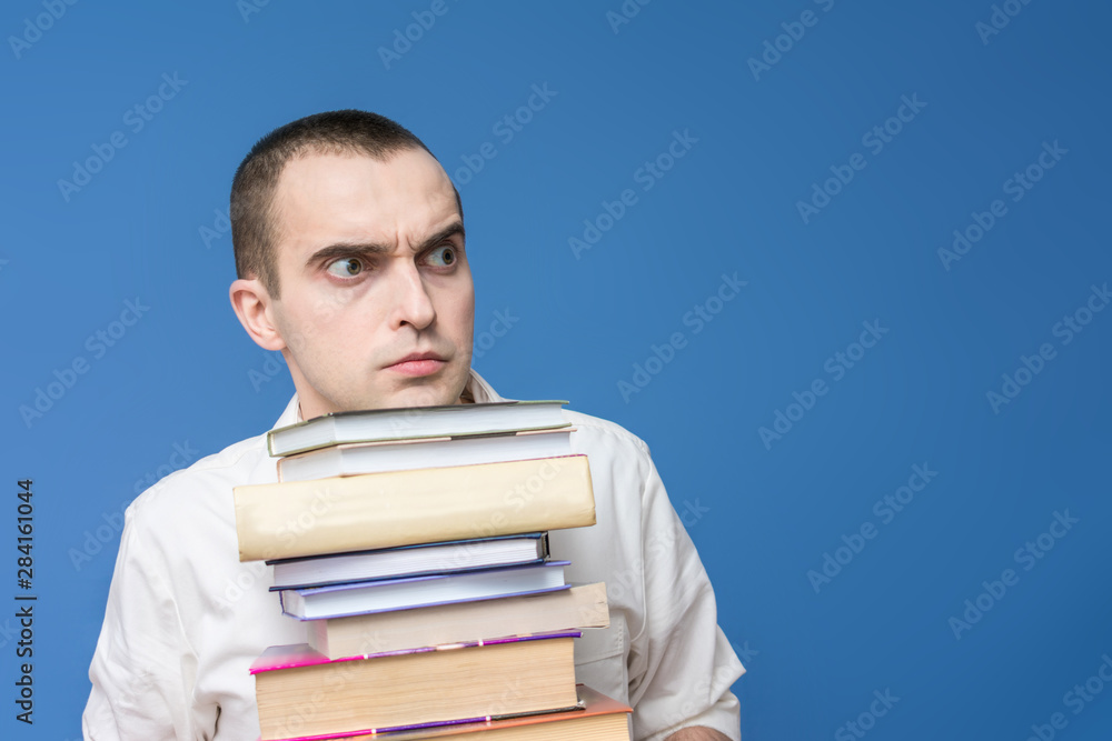 Guy with heavy books, close up, blue background, copy space, the concept of heavy loads in education Guy with heavy books, close up, blue background, copy space, the concept of heavy loads in education