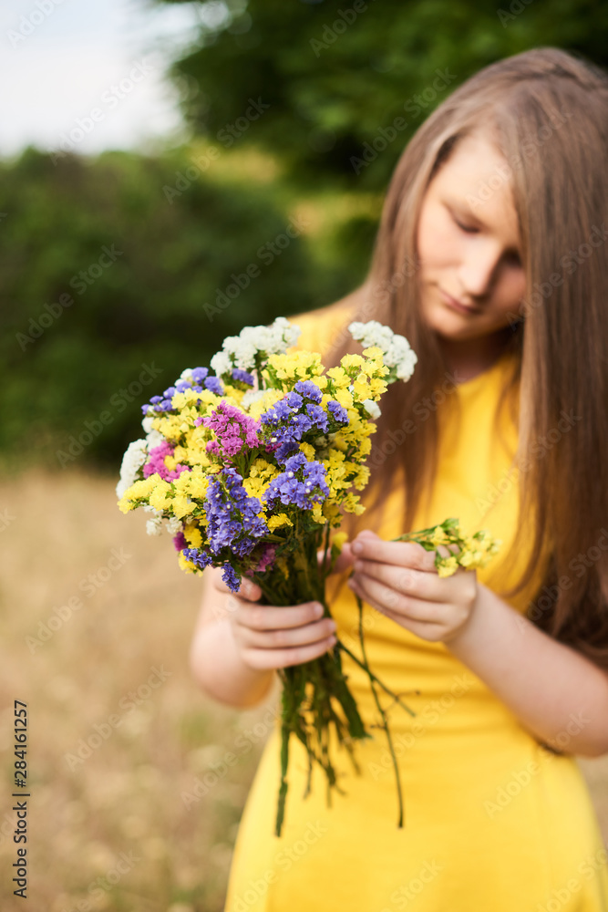young girl standing at outdoor park with bouquet of wildflowers