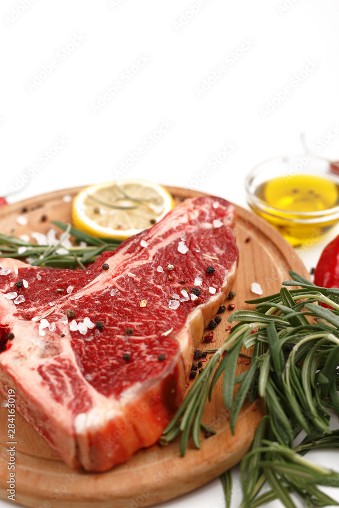 Raw t-bone steak on a wooden board with rosemary and spices on a white background. Top view.