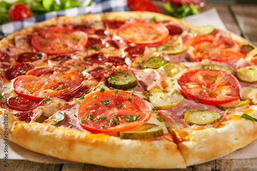 Pizza in half with salami, another - ham with pickled cucumbers and tomatoes sliced on wooden boards with vegetables