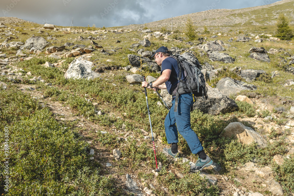 Man Hiking with backpack during the ascent of the peak in the summer. Concept trekking trips and active life with nature