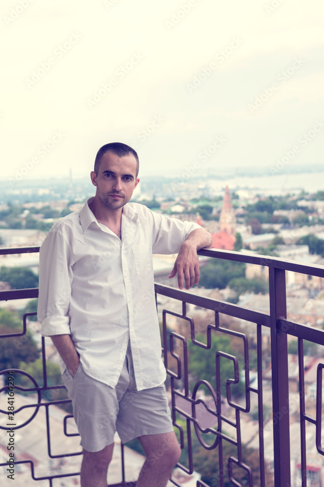 Attractive man, looking into the distance, standing on a beautiful terrace, toned