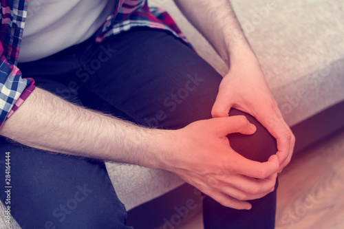Pain in the foot, man holds hands to his knee join, close up