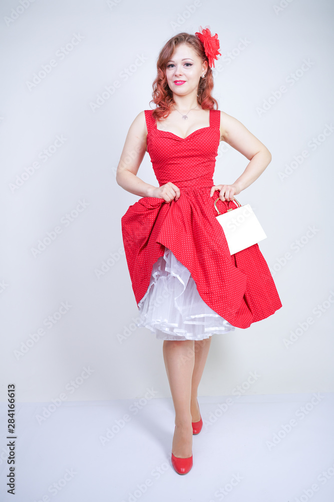 Beautiful redheaded girl in red midi pinup style dress isolated on white studio background standing alone Beautiful redheaded girl in red midi pinup style dress isolated on white studio background standing alone