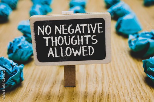 Handwriting text writing No Negative Thoughts Allowed. Concept meaning Always positive motivated inspired good vibes Stand blackboard with white words behind blurry blue paper lobs woody floor photo