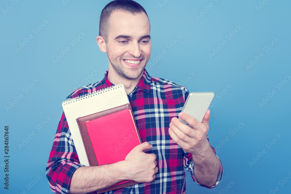 Happy school teacher or student with books, looking at smartphone screen, portrait, blue background, copy space, slogan Happy school teacher or student with books, looking at smartphone screen, portrait, blue background, copy space, slogan