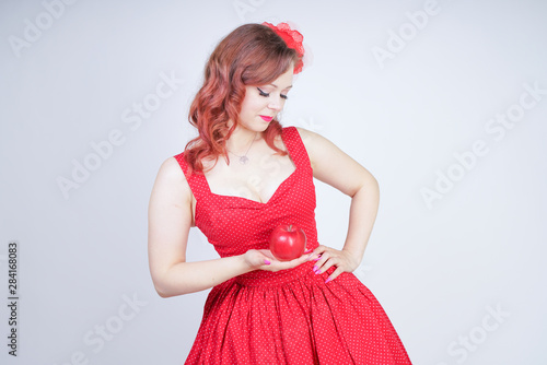 Sexy young pin-up girl holding red apple in her hand on white studio isolated background alone