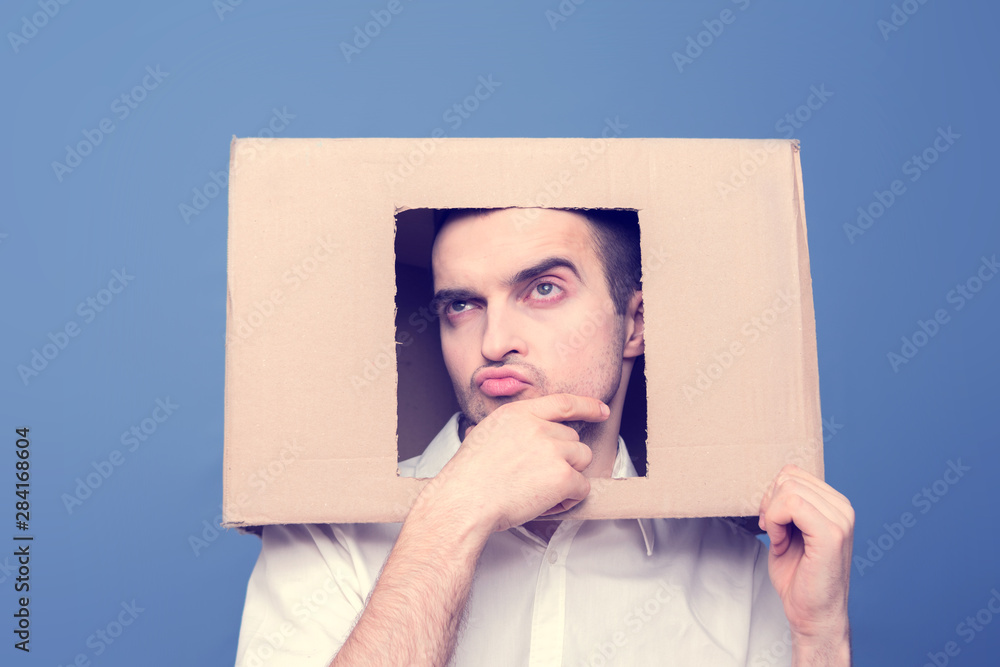 Thoughtful man with box on head, front view, emotions concept human, blue background Thoughtful man with box on head, front view, emotions concept human, blue background