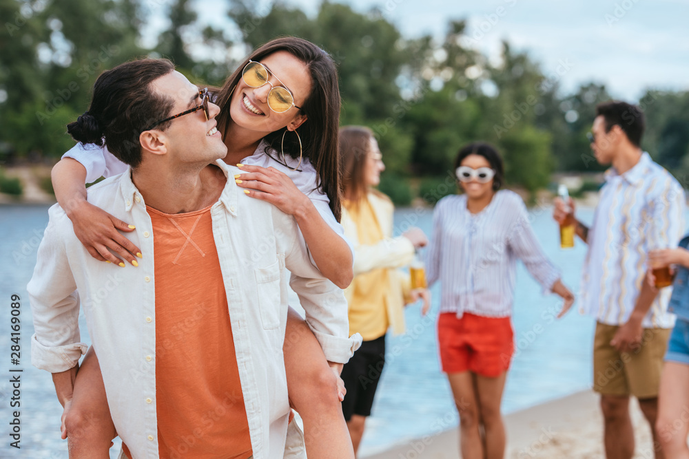 handsome young man piggybacking girlfriend while having fun on beach together with multicultural friends handsome young man piggybacking girlfriend while having fun on beach together with multicultural friends