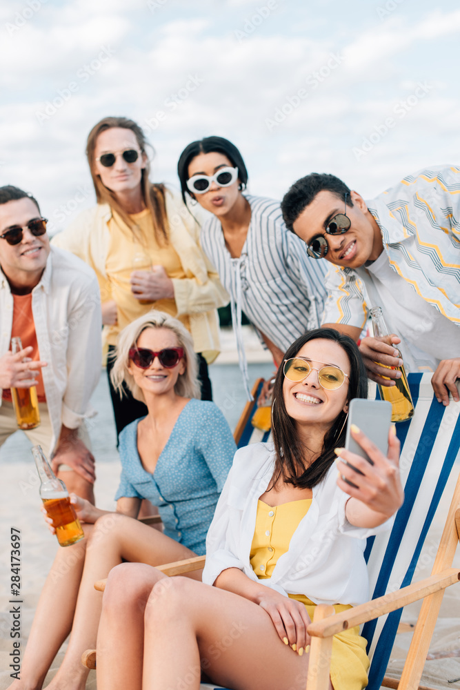 cheerful multicultural friends taking selfie while drinking beer and having fun on beach cheerful multicultural friends taking selfie while drinking beer and having fun on beach