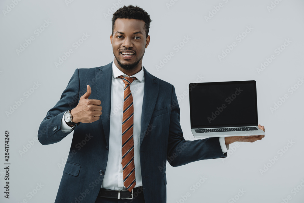 cheerful african american man holding laptop with blank screen and showing thumb up isolated on grey cheerful african american man holding laptop with blank screen and showing thumb up isolated on grey
