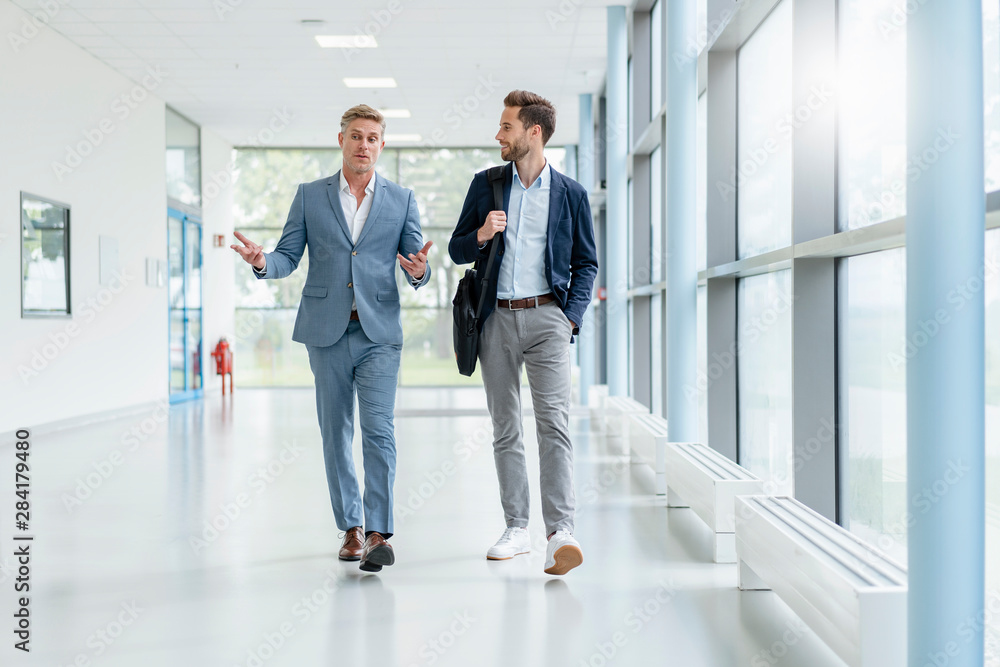 Two businessmen walking and talking in a passageway Two businessmen walking and talking in a passageway