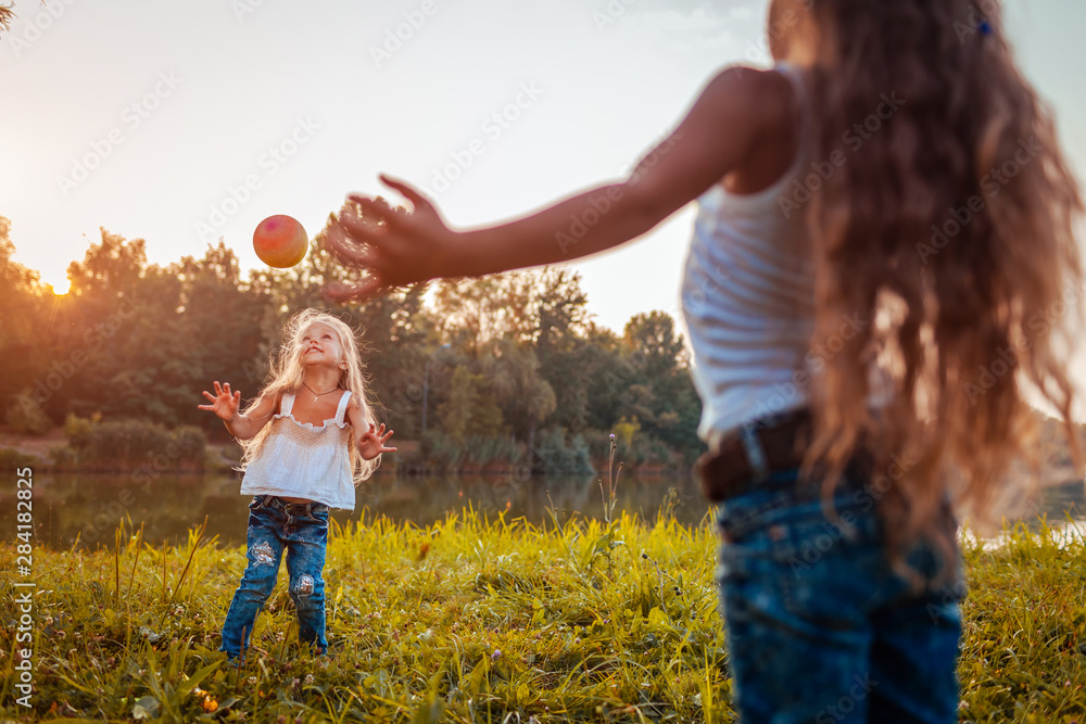 Fototapeta premium Little girls playing with ball in summer park. Kids having fun outdoors.