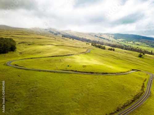 A drone landscape, angled view of cars traveling on the dangerous paved road leading up mount Haleakala. Mount Haleakala is a volcano stationed above the clouds on the island of Maui, Hawaii.