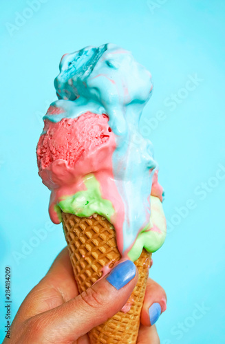 Woman's hand holding ice-cream cone with melting ice cream in front of blue background