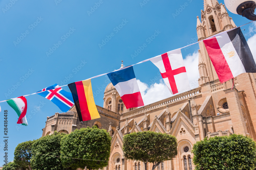 International flags of many countries fly outside a Roman Catholic church building.
