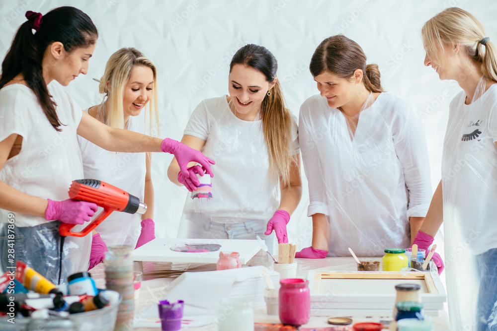 Woman painter dropping water on canvas while creating fluid acrylic abstract painting in art therapy class, hair dryer in her hand