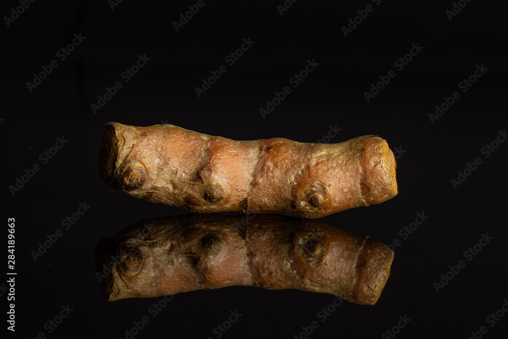 One whole pungent bright turmeric rhizome isolated on black glass One whole pungent bright turmeric rhizome isolated on black glass