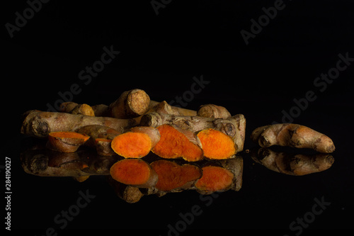 Group of lot of whole three slices of bright turmeric rhizome isolated on black glass