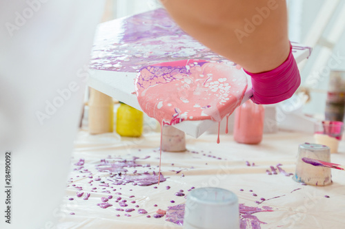 Woman painter holding hair dryer while female beginnres studying creating fluid acrylic abstract painting in art therapy class, dropping paints on canvas. Teamwork, study, art therapy concept. photo