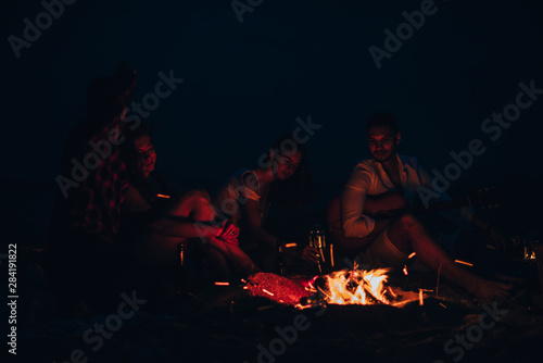 People sit at night round a bright bonfire on the beach