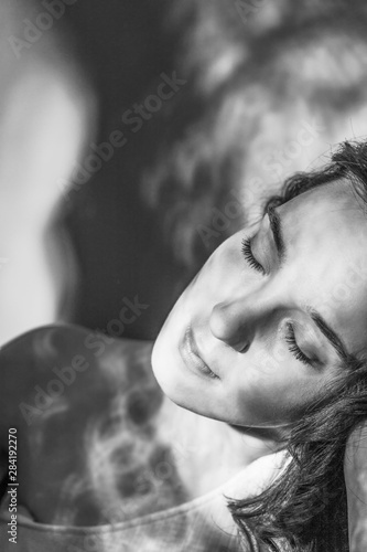 Beautiful young brunette woman with a shadows on face. Black and white portrait. Closed eyes. Copy space