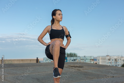 Slim athletic girl performs stretching exercises on the roof of an unfinished building, urban background. Enjoys silence and freedom.	