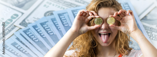 Young red-haired curly girl over dollar background holding piggy bank and rejoices gesturing. The concept of reliability of cash investments and insurance.