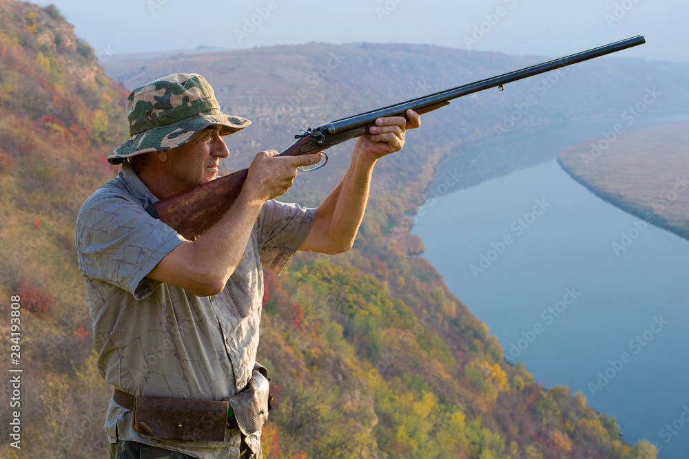 Fototapeta premium Hunter with a german drathaar and spaniel, pigeon hunting with dogs against the backdrop of a beautiful evening lake. 