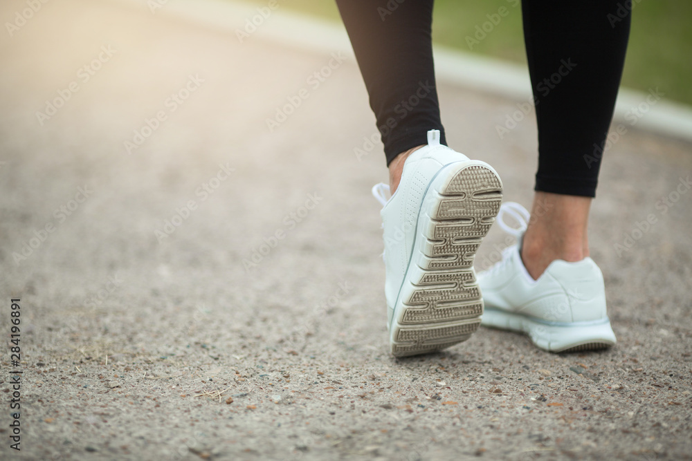 legs of a woman in white sneakers in the summer on the road