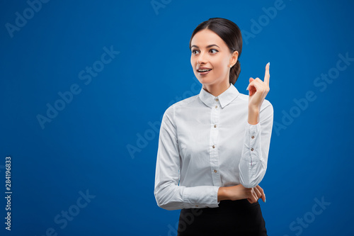 Young businesswoman smiling while coming up with an idea and looking to the left, isolated on blue background.