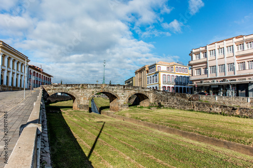 Bridge over river with green grass and old buildings of the city hall of the historic city of Sao Joao del Rey in the state of Minas Gerais, Brazil