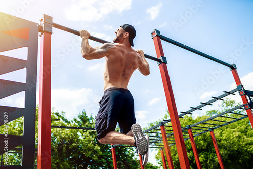 Brutal athletic man making pull-up exercises on a crossbar at outdoor streeet gym. Back view. photo
