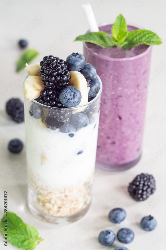 Smoothies of banana, blueberry, blackberry, oatmeal and yogurt and ingredients in two glasses on a light background Smoothies of banana, blueberry, blackberry, oatmeal and yogurt and ingredients in two glasses on a light background