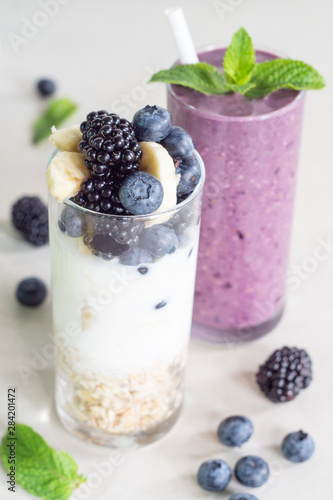 Smoothies of banana  blueberry  blackberry  oatmeal and yogurt and ingredients in two glasses on a light background