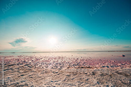 pink lake and sandy beach with a sea bay under a blue sky with clouds