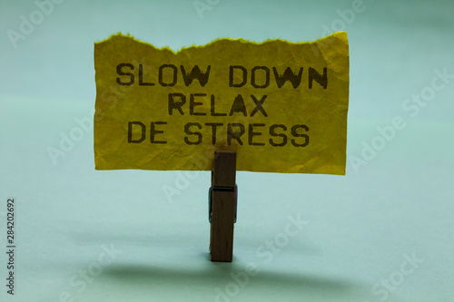 Text sign showing Slow Down Relax De Stress. Conceptual photo Have a break reduce stress levels rest calm Paperclip hold torn yellow page written brown words sky blue background photo