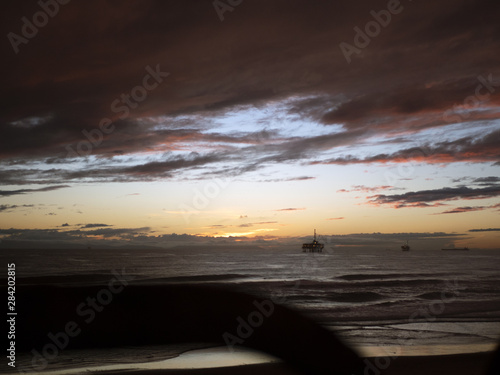 Sunset waves coming in, oil rig in silhouette.