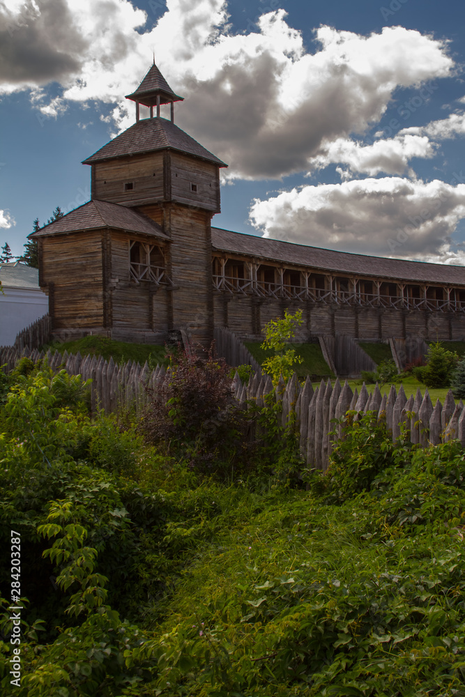 Bottom view of an old wooden fortress with a high watchtower against a blue cloudy sky, selective focus