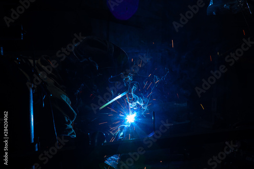 Professional welder works in helmet in industrial factory , manufacture linking and repair concept background. Sparks from welding at a construction.