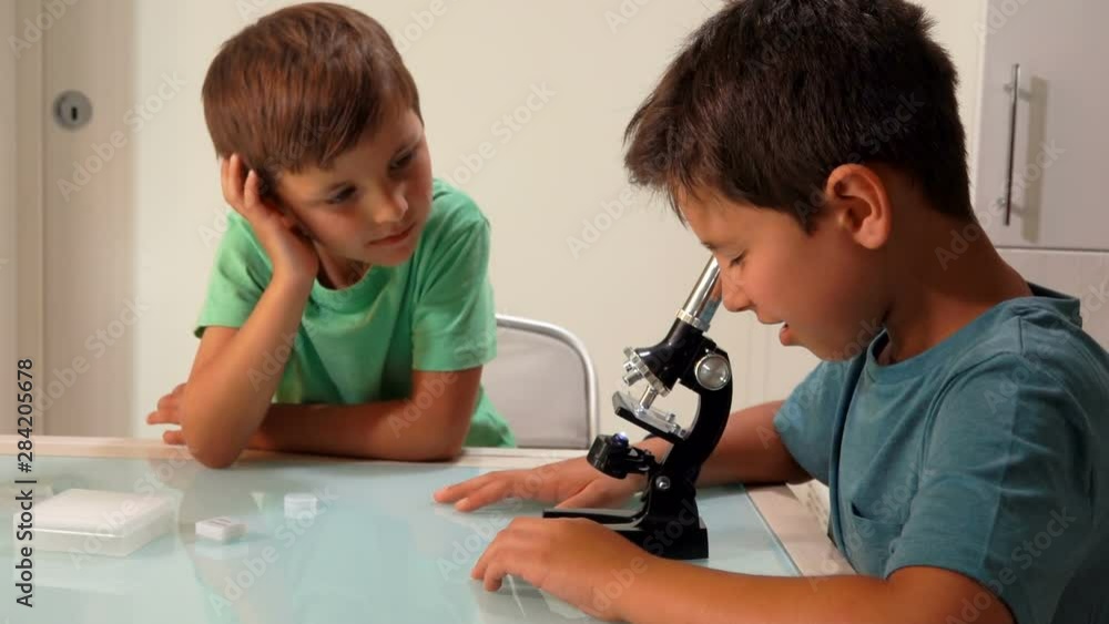 Older brother is looking through a microscope. The younger brother is waiting for his turn Older brother is looking through a microscope. The younger brother is waiting for his turn