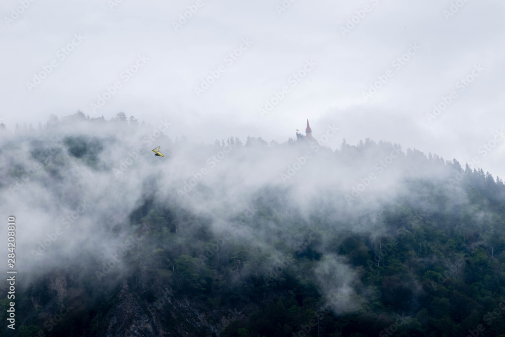 Mysterious view of forest on the mountain, castle and deltaplan in the thick fog