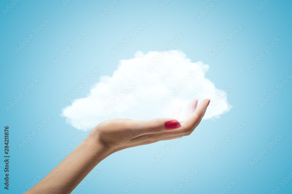 Female hand holding white cloud on blue background Female hand holding white cloud on blue background