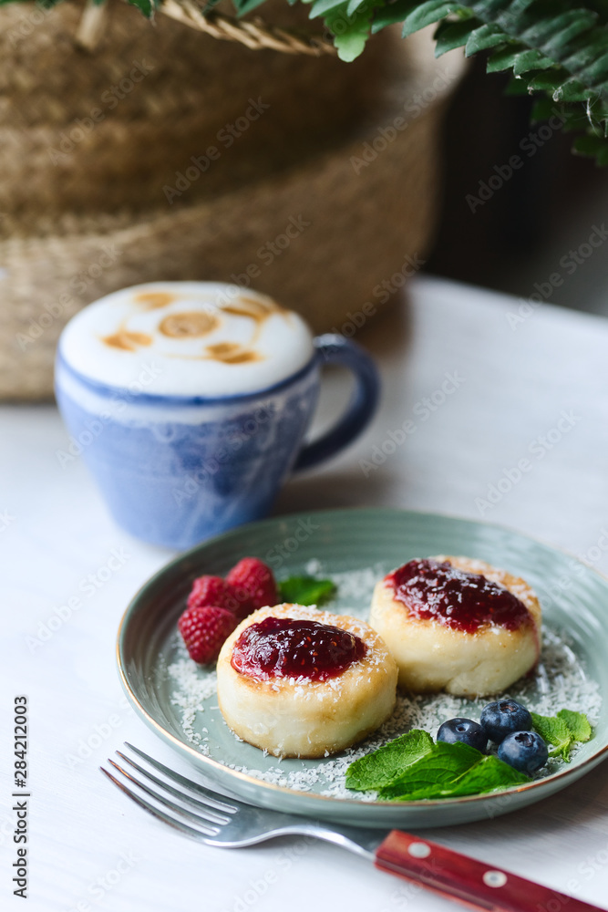 Cheesecakes with raspberry jam, berries and mint leaves served with a cup of latte