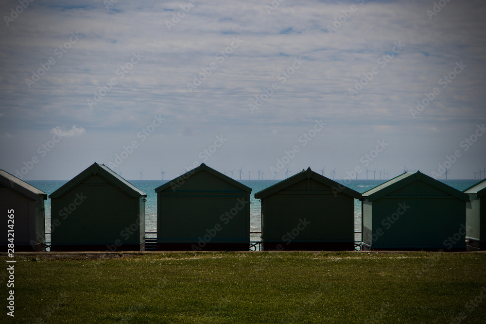 Obraz premium seascape of beach huts with wind turbines on the horizon